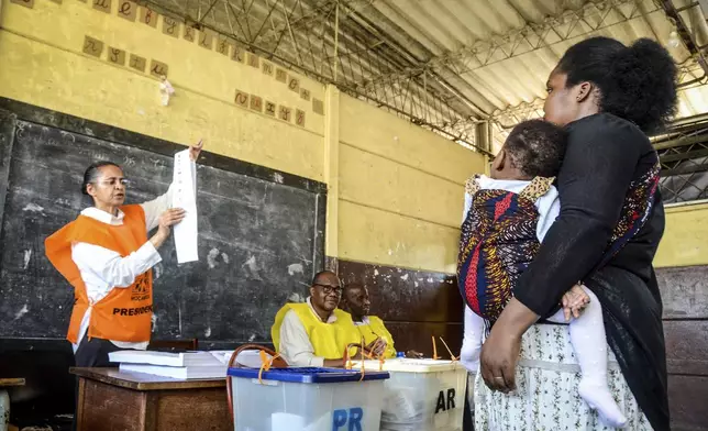 A woman carries a child at a polling station to vote in general elections in Maputo, Mozambique, Wednesday, Oct. 9, 2024. (AP Photo/Carlos Equeio)