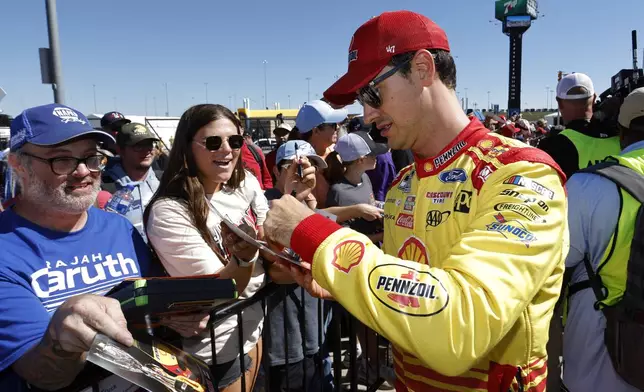 Joey Logano, right, gives autographs before a NASCAR Cup Series auto race at Kansas Speedway in Kansas City, Kan., Sunday, Sept. 29, 2024. (AP Photo/Colin E. Braley)