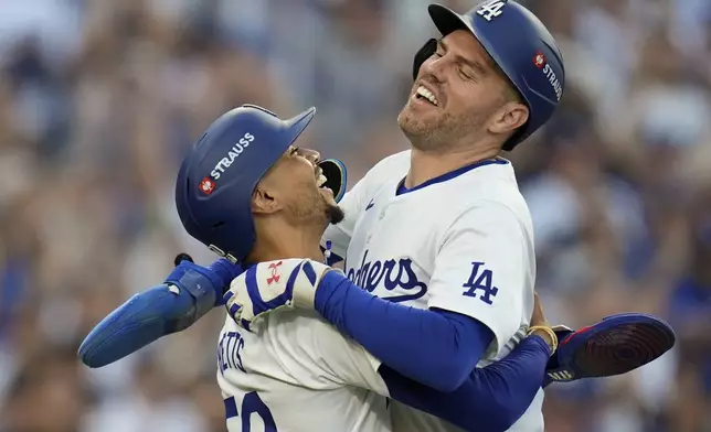 Los Angeles Dodgers' Freddie Freeman, right, and Mookie Betts celebrate after they scored on a single by Max Muncy during the first inning in Game 1 of a baseball NL Championship Series against the New York Mets, Sunday, Oct. 13, 2024, in Los Angeles. (AP Photo/Gregory Bull)