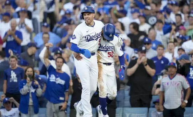 Los Angeles Dodgers' Freddie Freeman, left, and Mookie Betts celebrate after they scored on a single by Max Muncy during the first inning in Game 1 of a baseball NL Championship Series against the New York Mets, Sunday, Oct. 13, 2024, in Los Angeles. (AP Photo/Ashley Landis)