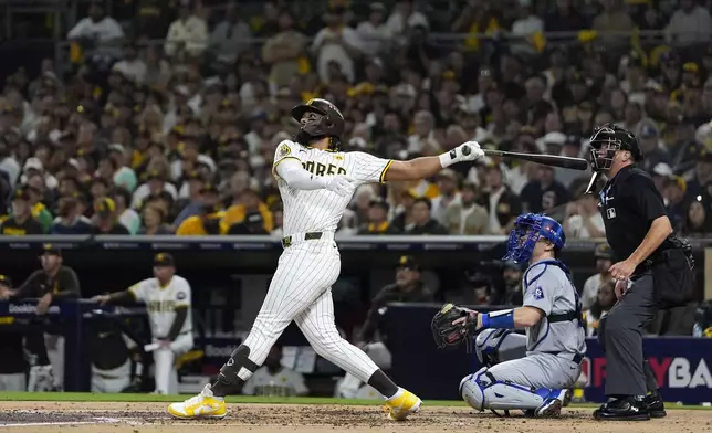 San Diego Padres' Fernando Tatis Jr., left, follows through on his two-run home run as Los Angeles Dodgers catcher Will Smith, center, and home plate umpire Cory Blaser watch during the second inning in Game 3 of a baseball NL Division Series, Tuesday, Oct. 8, 2024, in San Diego. (AP Photo/Gregory Bull)