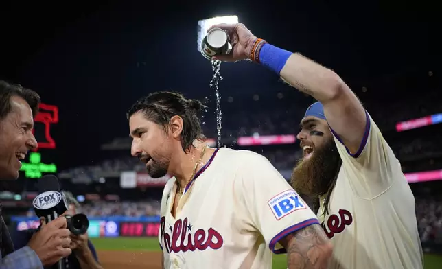 Philadelphia Phillies' Brandon Marsh, right, pours water over Nick Castellanos, center while he is interviewed after the Phillies won Game 2 of a baseball NL Division Series against the New York Mets, Sunday, Oct. 6, 2024, in Philadelphia. (AP Photo/Matt Slocum)