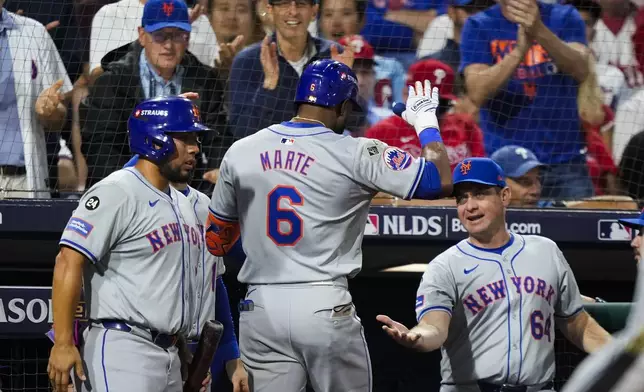 New York Mets' Starling Marte (6) celebrates after hitting an RBI sacrifice fly with New York Mets manager Carlos Mendoza (64) during the eighth inning of Game 1 of a baseball NL Division Series, Saturday, Oct. 5, 2024, in Philadelphia. (AP Photo/Matt Slocum)