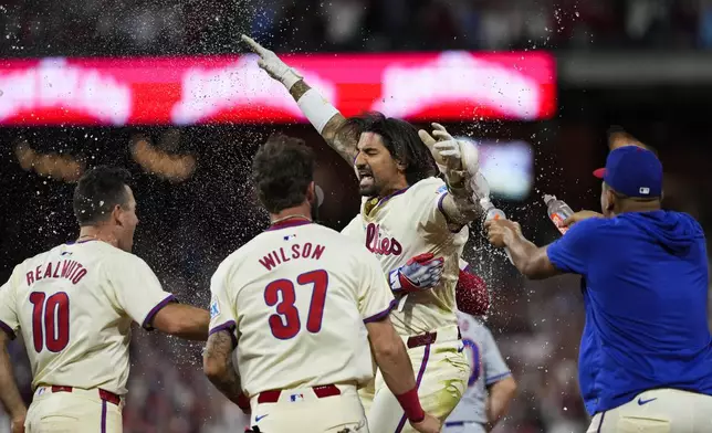 Philadelphia Phillies' Nick Castellanos celebrates with teammates his one-run single against New York Mets pitcher Tylor Megill during the ninth inning to win Game 2 of a baseball NL Division Series, Sunday, Oct. 6, 2024, in Philadelphia. (AP Photo/Matt Slocum)