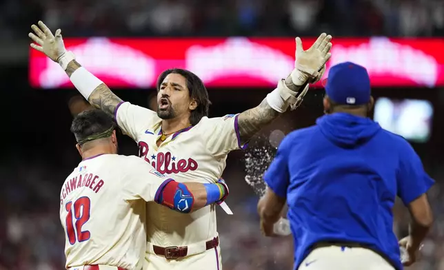 Philadelphia Phillies' Nick Castellanos celebrates with Kyle Schwarber and teammates his one-run single against New York Mets pitcher Tylor Megill during the ninth inning to win Game 2 of a baseball NL Division Series, Sunday, Oct. 6, 2024, in Philadelphia. (AP Photo/Matt Slocum)