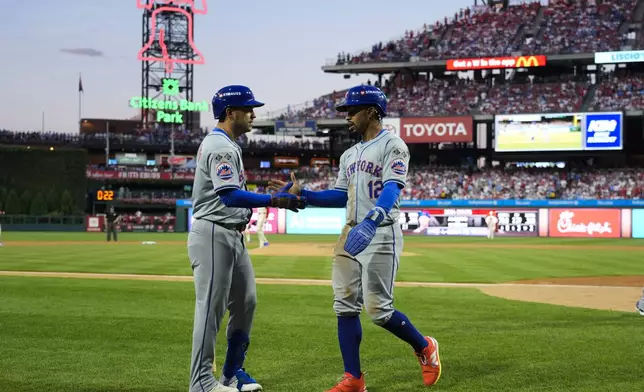 New York Mets' Francisco Lindor (12) celebrates with Jose Iglesias after scoring on a hit by Brandon Nimmo during the eighth inning of Game 1 of a baseball NL Division Series against the Philadelphia Phillies, Saturday, Oct. 5, 2024, in Philadelphia. (AP Photo/Chris Szagola)