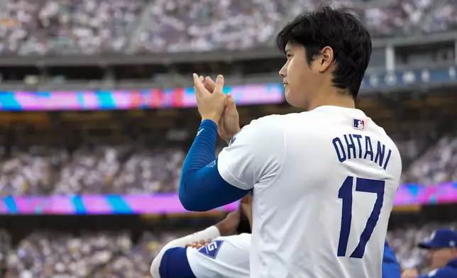 Los Angeles Dodgers' Shohei Ohtani applauds in the dugout during the second inning in Game 5 of a baseball NL Division Series against the San Diego Padres, Friday, Oct. 11, 2024, in Los Angeles. (AP Photo/Ashley Landis)