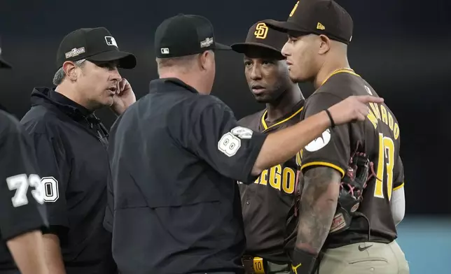 San Diego Padres left fielder Jurickson Profar, second from right, and third baseman Manny Machado talk to the umpires after items were thrown at Profar in the outfield during the seventh inning in Game 2 of a baseball NL Division Series against the Los Angeles Dodgers, Sunday, Oct. 6, 2024, in Los Angeles. (AP Photo/Ashley Landis)