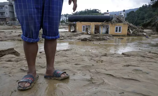 A man stands on a muddy plain next to a damaged structure in Kathmandu, Nepal, Monday, Sept. 30, 2024 in the aftermath of a flood caused by heavy rains . (AP Photo/Gopen Rai)