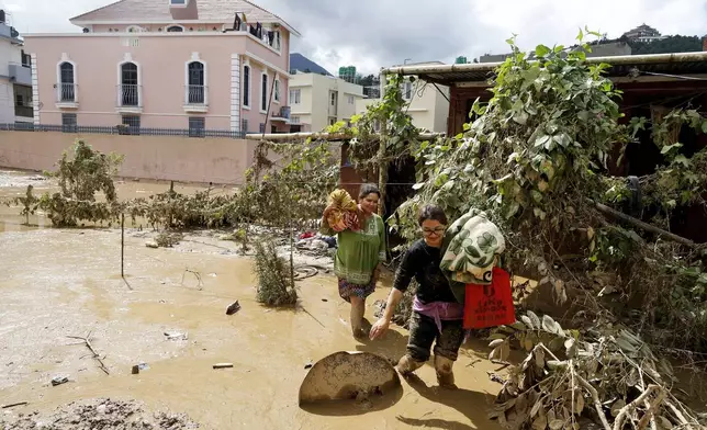 Women walk with their belongings in the mud in Kathmandu, Nepal, Monday, Sept. 30, 2024 in the aftermath of a flood caused by heavy rains. (AP Photo/Gopen Rai)