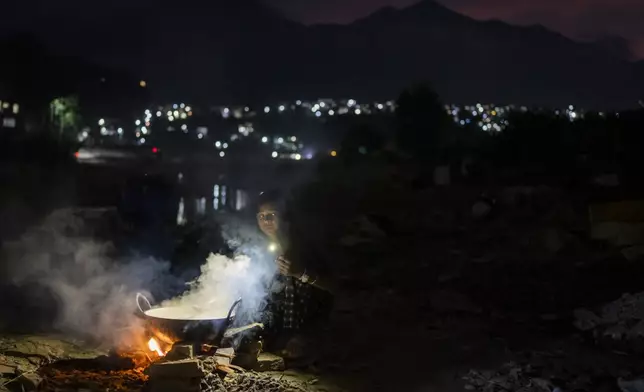 A woman cooks food near her makeshift shelter after her home was swept away by the flooding Bagmati River in Kathmandu, Nepal, on Tuesday, Oct. 1, 2024. (AP Photo/Niranjan Shrestha)