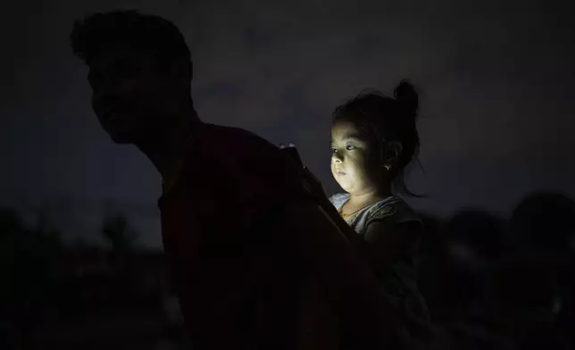 A man affected by the flood carries his child, playing with a mobile phone, as they walk towards their makeshift shelter in Kathmandu, Nepal, on Tuesday, Oct. 1, 2024. (AP Photo/Niranjan Shrestha)