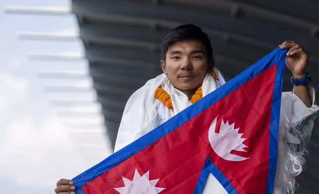 Nepalese mountaineer Nima Rinji Sherpa, the youngest person to scale all the world’s 14 highest peaks, waves Nepalese flag as his arrives at Tribhuvan International Airport in Kathmandu, Nepal, Monday, Oct. 14, 2024. (AP Photo/Niranjan Shrestha)