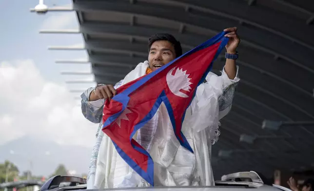 Nepalese mountaineer Nima Rinji Sherpa, the youngest person to scale all the world’s 14 highest peaks, waves Nepalese flag as hi arrives at Tribhuvan International Airport in Kathmandu, Nepal, Monday, Oct. 14, 2024. (AP Photo/Niranjan Shrestha)