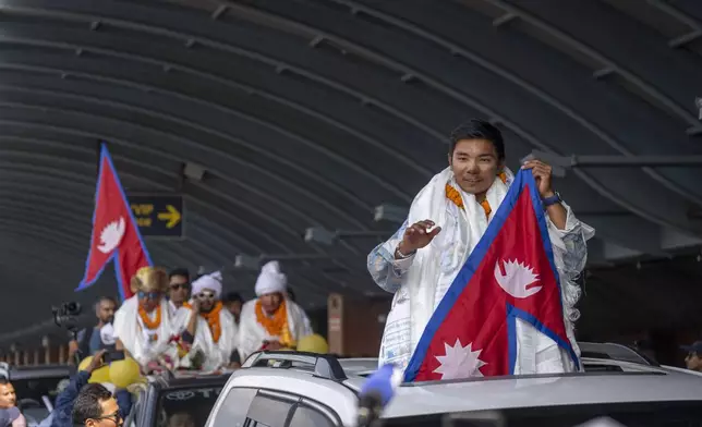 Nepalese mountaineer Nima Rinji Sherpa, the youngest person to scale all the world’s 14 highest peaks, waves Nepalese flag as his arrives at Tribhuvan International Airport in Kathmandu, Nepal, Monday, Oct. 14, 2024. (AP Photo/Niranjan Shrestha)