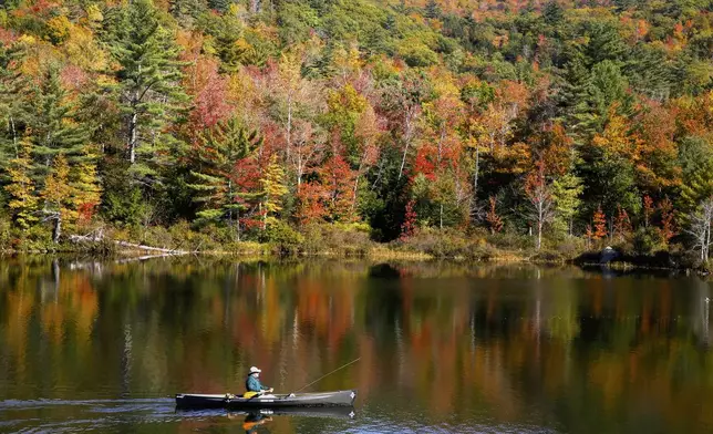 A fly fisherman paddles on a pond as fall foliage begins to show color in Campton, N.H., Sunday, Oct. 6, 2024. (AP Photo/Caleb Jones)