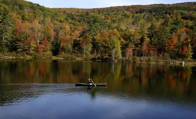 A fly fisherman paddles on a pond as fall foliage begins to show color in Campton, N.H., Sunday, Oct. 6, 2024. (AP Photo/Caleb Jones)