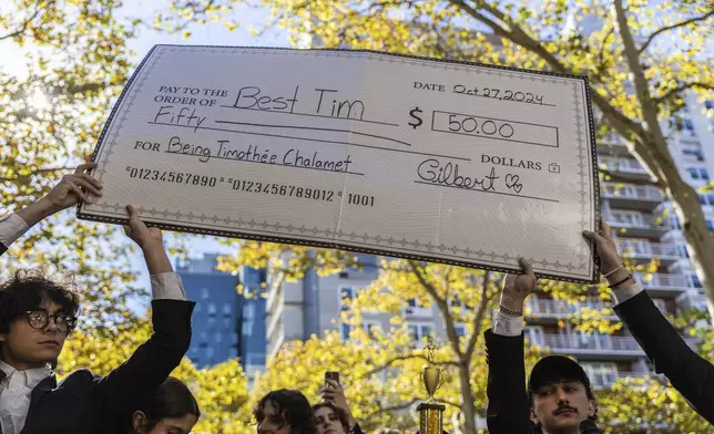 A giant cheque for the prize money is held aloft at the Timothee Chalamet lookalike contest near Washington Square Park, Sunday, Oct. 27, 2024, in New York. (AP Photo/Stefan Jeremiah)