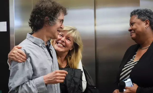 Hannele Ruohola-Baker hugs her husband American biochemist David Baker, 2024 Nobel Prize winner in Chemistry, at the University of Washington on Wednesday, Oct. 9, 2024, in Seattle. Lynda Stuart, executive director at the Institute for Protein Design, looks on at right. (AP Photo/Lindsey Wasson)