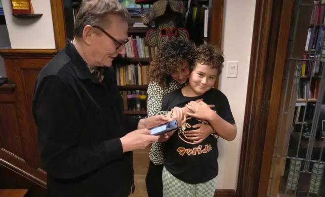 Nobel prize winner in Economics, James A. Robinson, looks over a selfie he made for the Nobel Foundation with his wife Dr. Maria Angelica Bautista, and son Adrian at their home in the Hyde Park neighborhood of Chicago, Monday, Oct. 14, 2024. (AP Photo/Charles Rex Arbogast)