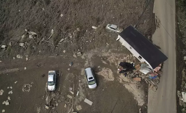 A destroyed mobile home and vehicles lay scattered across muddy land, Tuesday, Oct. 1, 2024, in Hendersonville, N.C., in the aftermath of Hurricane Helene. (AP Photo/Brittany Peterson)