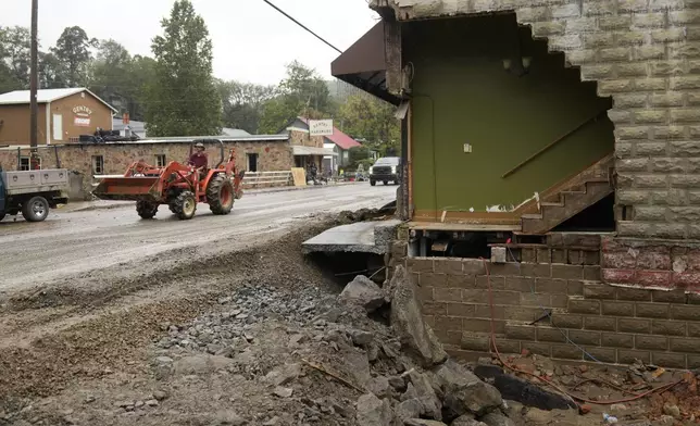 A person driving a front in loader passes a heavily one of several heavily damaged buildings along Bridge Street as clean up begins in the aftermath of Hurricane Helene Tuesday, Oct. 1, 2024, in Hot Springs, N.C. (AP Photo/Jeff Roberson)