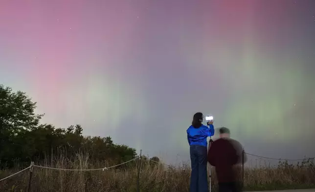 People watch as an aurora borealis, also known as the northern lights, lights up the night sky from Montrose Point, Thursday, Oct. 10, 2024, in Chicago. (Tyler Pasciak LaRiviere/Chicago Sun-Times via AP)