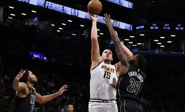 Denver Nuggets' Nikola Jokic (15), of Serbia, shoots against Brooklyn Nets' Dorian Finney-Smith (28) and Cam Thomas, left, during the third quarter of an NBA basketball game Tuesday, Oct. 29, 2024, in New York. (AP Photo/Jason DeCrow)