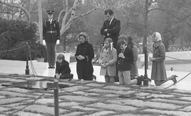 FILE - Sen. Edward Kennedy, back, stands behind the widow of former Senator Robert F. Kennedy, Mrs. Ethel Kennedy, second left, with her five children, and his wife Joan, right, as they pause at the grave of assassinated President John F. Kennedy in Arlington National Cemetery, Nov. 20, 1970, in Arlington, Va. (AP Photo/Bob Daugherty, File)