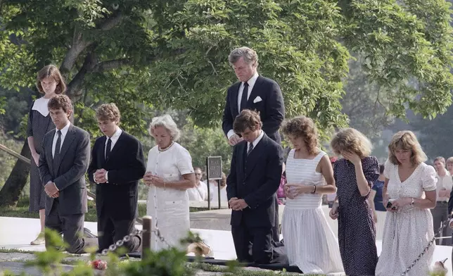 FILE - Members of the Kennedy family kneel at the grave site of the late President John F. Kennedy at Arlington National Cemetery after they visited the grave of the late Robert F. Kennedy nearby, on the anniversary of his death 16 years ago, June 6, 1984. From left: Emily and Robert F. Kennedy, Jr.; Chris Kennedy; Ethel Kennedy; Michael Kennedy and Kathleen Kennedy, the wife and children of Robert Kennedy. Sen. Edward M. Kennedy (D-Mass.) stands at back. (AP Photo/Barry Thumma, File)