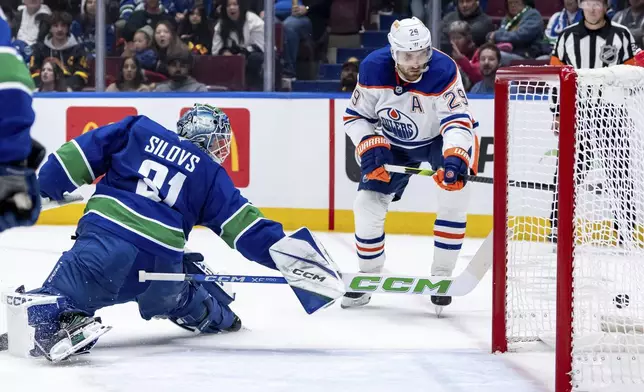 Vancouver Canucks goaltender Arturs Silovs, left, watches Edmonton Oilers' Leon Draisaitl (29) misses the net during first-period preseason NHL hockey game action in Vancouver, British Columbia, Friday, Oct. 4, 2024. (Ethan Cairns/The Canadian Press via AP)