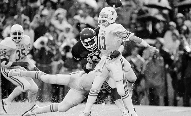 FILE - In this Oct. 13, 1984, file photo, Texas quarterback Todd Dodge (13) gets the ball away as he is tackled by Oklahoma's Darell Reed (40) during the third period of an NCAA college football game in Dallas. The pass fell incomplete. The game ended in a 15-15 tie. (AP Photo/Ron Ennis, File)