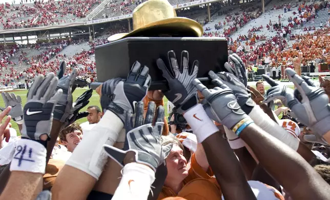 FILE - In this Oct. 11, 2008, file photo, Texas coach Mack Brown, center under trophy, and the Longhorns celebrate their 45-35 win over Oklahoma win with the "Golden Hat Trophy" after an NCAA college football game in Dallas. (AP Photo/ University of Texas, Jim Sigmon, Pool, File)