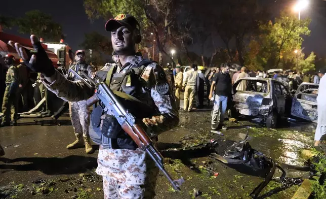 A paramilitary soldier gestures toward media as security officials examine the site of an explosion that caused injures and destroyed vehicles at outside the Karachi airport, Pakistan, Monday, Oct. 7, 2024. (AP Photo/Fareed Khan)