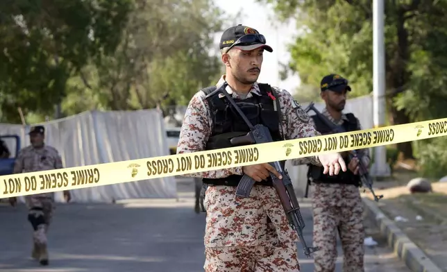 Security officials stand guard at the site of an explosion that caused injures and destroyed vehicles outside the Karachi airport, Pakistan, Monday, Oct. 7, 2024. Pakistani Baloch separatists claim deadly bomb attack that killed 2 Chinese near Karachi airport. (AP Photo/Fareed Khan)