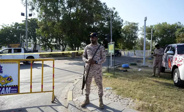 Security officials stand guard next to the site of an explosion that caused injures and destroyed vehicles outside the Karachi airport, Pakistan, Monday, Oct. 7, 2024. Pakistani Baloch separatists claim deadly bomb attack that killed 2 Chinese near Karachi airport. (AP Photo/Fareed Khan)