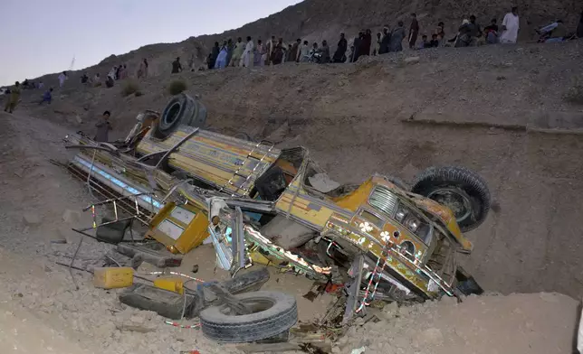 Local residents gather beside the wreckage of a bus that fell into a ravine, near Quetta, the capital of Balochistan province, Pakistan, Thursday, Oct. 3, 2024. A speeding bus carrying wedding guests plunged into a ravine in southwestern Pakistan on Thursday, killing at least seven people, officials and rescuers said. (AP Photo/Arshad Butt)