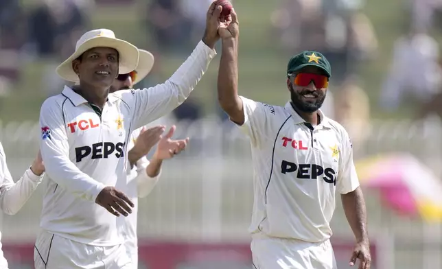 Pakistan's Noman Ali, left, and Sajid Khan display the ball jointly as they walk off the field on the end of England's second innings during the day three of third test cricket match between Pakistan and England, in Rawalpindi, Pakistan, Saturday, Oct. 26, 2024. (AP Photo/Anjum Naveed)