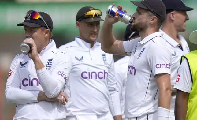 England's Chris Woakes, second right, and Ollie Pope, left, drink as they wait for third umpire decision regarding the dismissal of Pakistan's Salman Ali Agha during the second day of the first test cricket match between Pakistan and England, in Multan, Pakistan, Tuesday, Oct. 8, 2024. (AP Photo/Anjum Naveed)