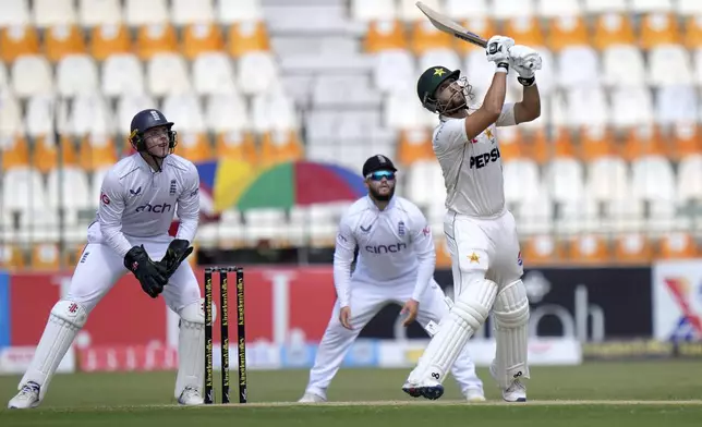 Pakistan's Salman Ali Agha, right, follows the ball after playing a shot as England's Jamie Smith, left, and Ben Duckett watch during the second day of the first test cricket match between Pakistan and England, in Multan, Pakistan, Tuesday, Oct. 8, 2024. (AP Photo/Anjum Naveed)