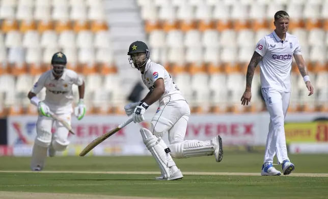 Pakistan's Abdullah Shafique, center, and Shan Masood, left, run between the wickets as England's Brydon Carse watches during the first day of the first test cricket match between Pakistan and England, in Multan, Pakistan, Monday, Oct. 7, 2024. (AP Photo/Anjum Naveed)