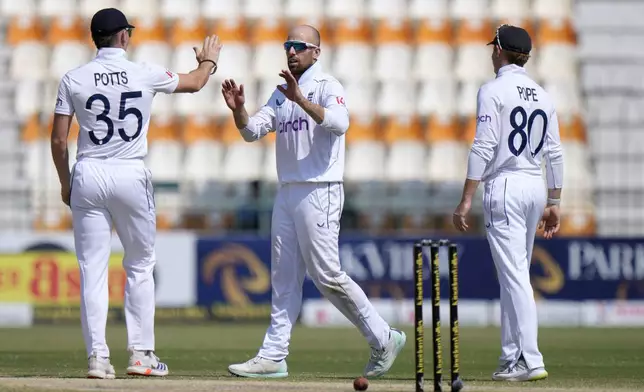 England's Jack Leach, center, celebrates with Ollie Pope after taking the wicket of Pakistan's Shaheen Shah Afridi during the fifth day of the first test cricket match between Pakistan and England, in Multan, Pakistan, Friday, Oct. 11, 2024. (AP Photo/Anjum Naveed)