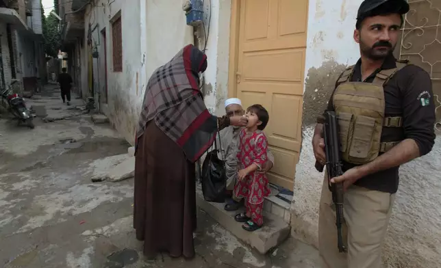 A police officer stands guard as a health worker, center, administers a polio vaccine to a child in a neighbourhood of Peshawar, Pakistan, Monday, Oct. 28, 2024. (AP Photo/Mohammad Sajjad)