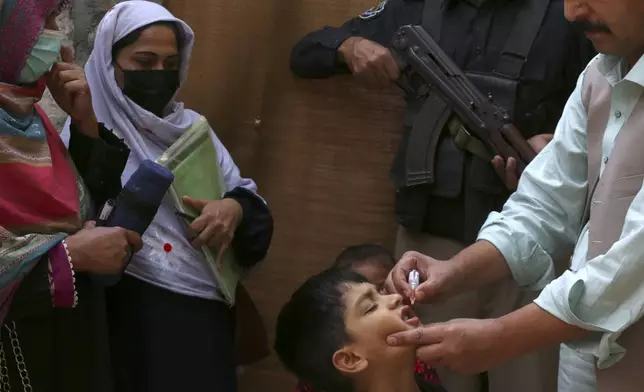 A police officer stands guard as a health worker, right, administers a polio vaccine to a child in a neighbourhood of Peshawar, Pakistan, Monday, Oct. 28, 2024. (AP Photo/Mohammad Sajjad)