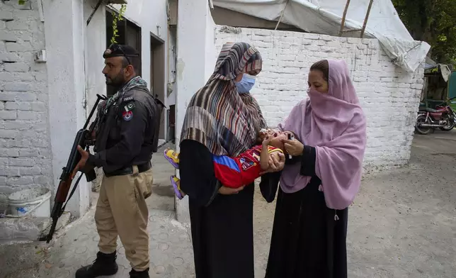 FILE -A police officer stands guard as a health worker, right, administers a polio vaccine to a child in a neighborhood of Peshawar, Pakistan, Sept. 9, 2024. (AP Photo/Muhammad Sajjad, File)