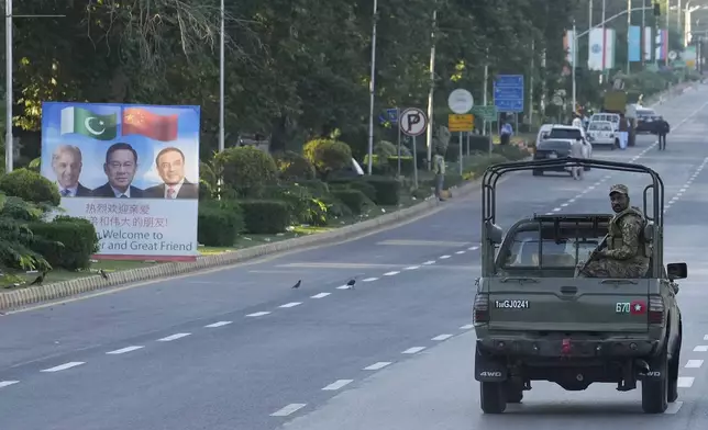 An army vehicle moves past a welcoming billboard with portraits of China's Premier Li Qiang, center, Pakistan's Prime Minister Shehbaz Sharif and President Asif Ali Zardari, displayed along a road leading to the venue of the upcoming Shanghai Cooperation Organization (SCO) summit in Islamabad, Pakistan, Sunday, Oct. 13, 2024. (AP Photo/Anjum Naveed)