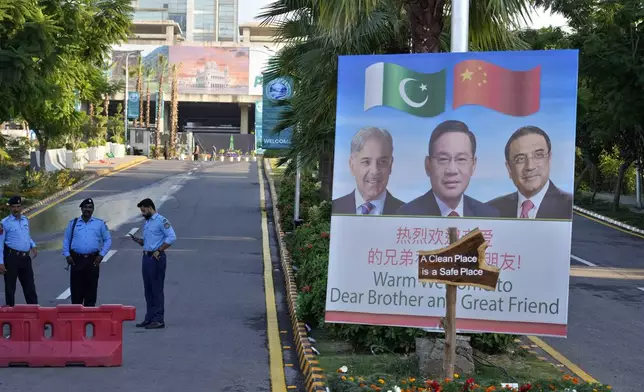 Police officers stand guard next to a welcoming billboard with portraits of China's Premier Li Qiang, center, Pakistan's Prime Minister Shehbaz Sharif and President Asif Ali Zardari, displayed at a road leading to the venue of the upcoming Shanghai Cooperation Organization (SCO) summit in Islamabad, Pakistan, Sunday, Oct. 13, 2024. (AP Photo/Anjum Naveed)