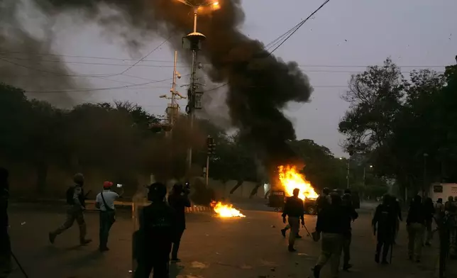 Police and paramilitary soldiers chase supporters of the Tehreek-e-Labbaik Pakistan party who setting on fire a police vehicle during clashes in Karachi, Pakistan, Sunday, Oct. 13, 2024. (AP Photo/Fareed Khan)