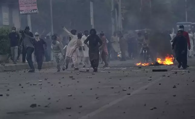 Supporters of the Tehreek-e-Labbaik Pakistan party burn bushes and throw stones towards police during clashes following protestors tried to break through a security barricade, in Karachi, Pakistan, Sunday, Oct. 13, 2024. (AP Photo/Fareed Khan)