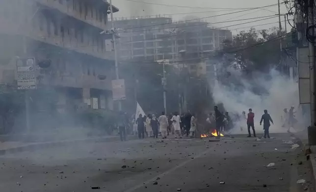 Supporters of the Tehreek-e-Labbaik Pakistan party burn bushes as police fire tear gas shell to disperse them during clashes in Karachi, Pakistan, Sunday, Oct. 13, 2024. (AP Photo/Fareed Khan)